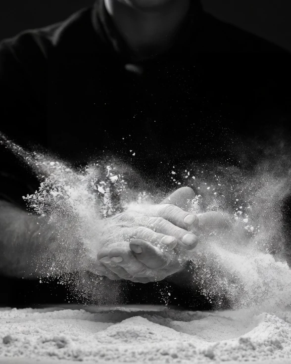 Silhouette en noir qui claque les mains dans un nuage de farine au-dessus d'un tas posé sur la table