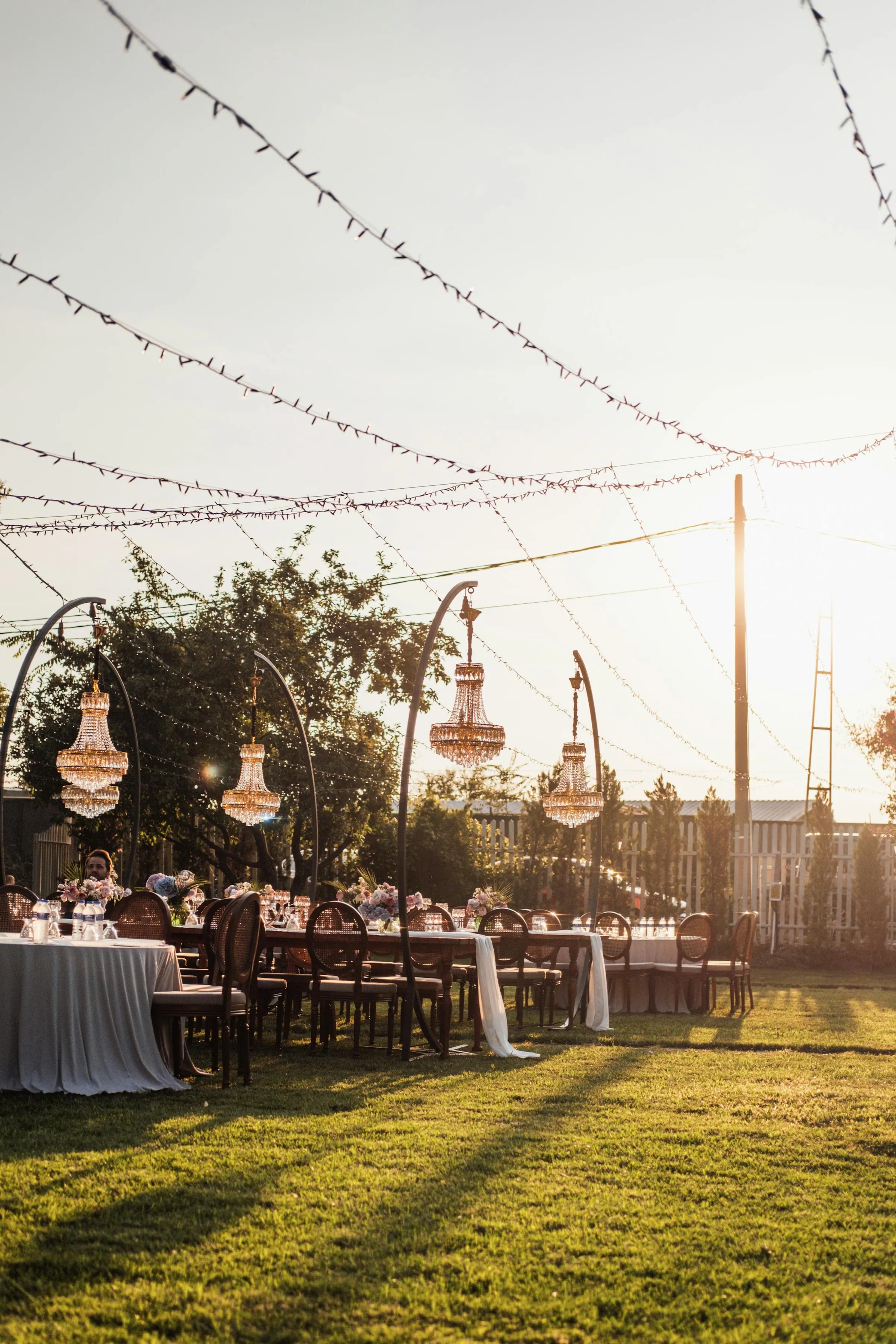 Réception de mariage en extérieur — tables dressées sous chandeliers en lumière de fin de journée